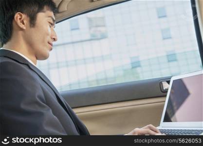 Businessman in Back Seat of Car Typing on Laptop, Low Angle View