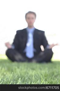 Businessman in black suit is meditating in the green grass with the sun behind him