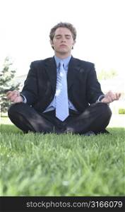 Businessman in black suit is sitting in meditation in the green grass