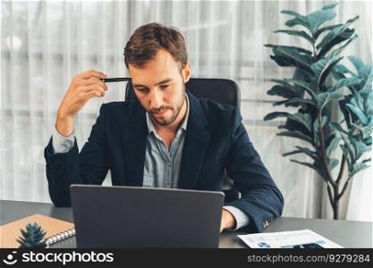 Businessman in black suit working on laptop at his workspace desk. Smart executive researching financial data and planning marketing strategy on corporate laptop at modern workplace. Entity. Businessman in black suit working on laptop at his workspace desk. Entity