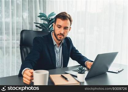 Businessman in black suit working on laptop at his workspace desk. Smart executive researching financial data and planning marketing strategy on corporate laptop at modern workplace. Entity. Businessman in black suit working on laptop at his workspace desk. Entity