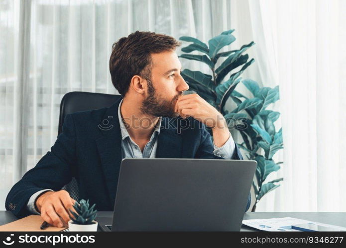 Businessman in black suit working on laptop at his workspace desk. Smart executive researching financial data and planning marketing strategy on corporate laptop at modern workplace. Entity. Businessman in black suit working on laptop at his workspace desk. Entity