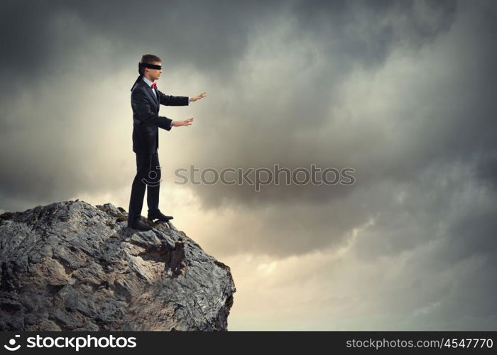 Businessman in blindfold. Image of businessman in blindfold standing on edge of mountain