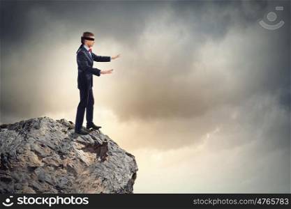 Businessman in blindfold. Image of businessman in blindfold standing on edge of mountain