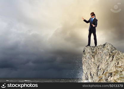 Businessman in blindfold. Image of businessman in blindfold standing on edge of mountain