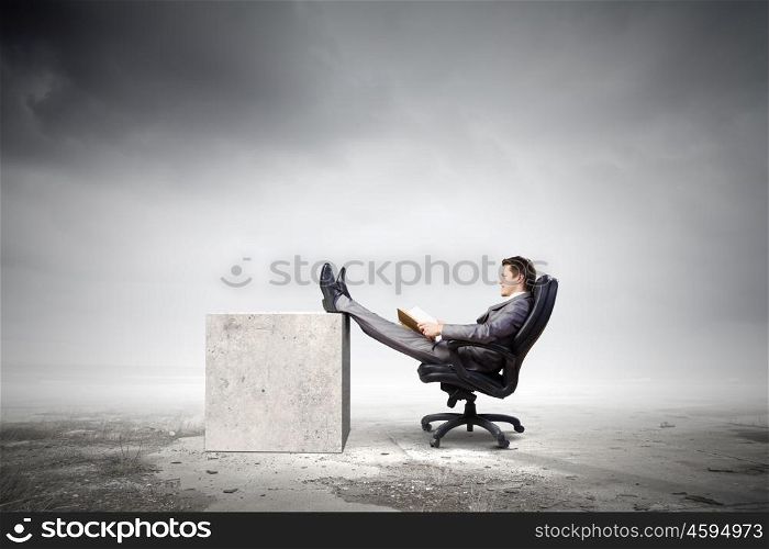 Businessman in chair. Young businessman sitting in chair with book in hands