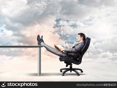 Businessman in chair. Young businessman sitting in chair with book in hands