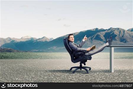 Businessman in chair. Young businessman sitting in chair with book in hands