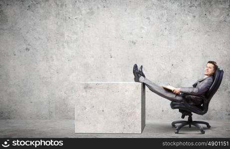 Businessman in chair. Young businessman sitting in chair with book in hands