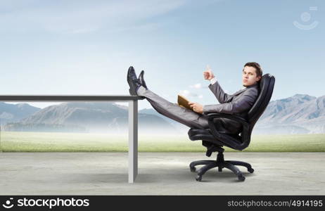 Businessman in chair. Young businessman sitting in chair with book in hands