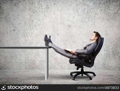 Businessman in chair. Young businessman sitting in chair with book in hands