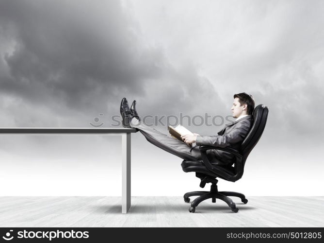 Businessman in chair. Young businessman sitting in chair with book in hands