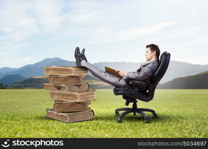 Businessman in chair. Young businessman sitting in chair with book in hands