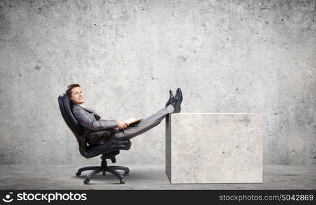 Businessman in chair. Young businessman sitting in chair with book in hands