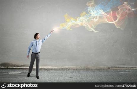 Businessman in concrete room. Businessman reaching hand to touch colorful fumes above head