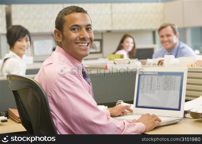 Businessman in cubicle using laptop and smiling