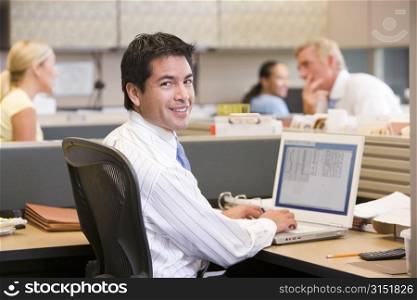 Businessman in cubicle with laptop smiling