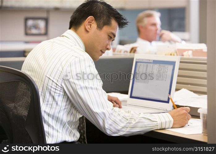 Businessman in cubicle with laptop writing