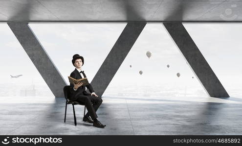 Businessman in cylinder reading book. Young businessman in office sitting in chair with old book in hands