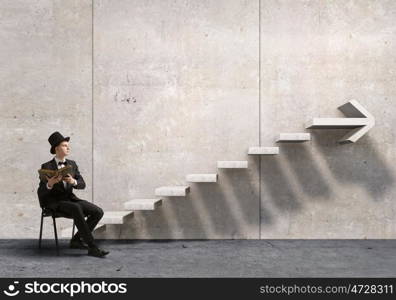 Businessman in cylinder reading book. Young businessman in office sitting in chair with old book in hands