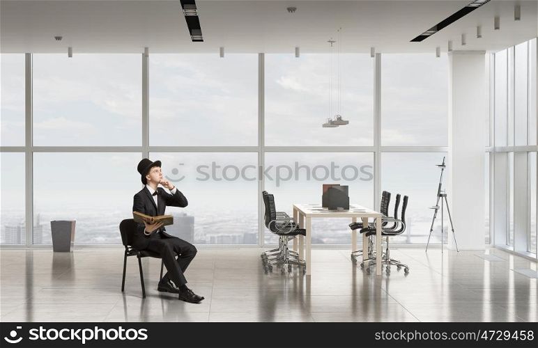 Businessman in cylinder reading book. Young businessman in office sitting in chair with old book in hands