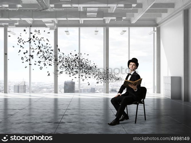 Businessman in cylinder reading book. Young businessman in office sitting in chair with old book in hands