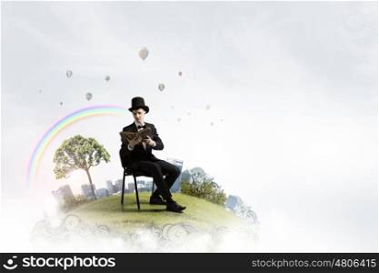 Businessman in cylinder reading book. Young businessman outdoor sitting in chair with old book in hands