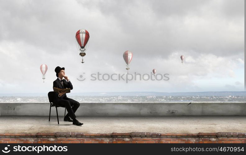 Businessman in cylinder reading book. Young businessman sitting in chair with old book in hands