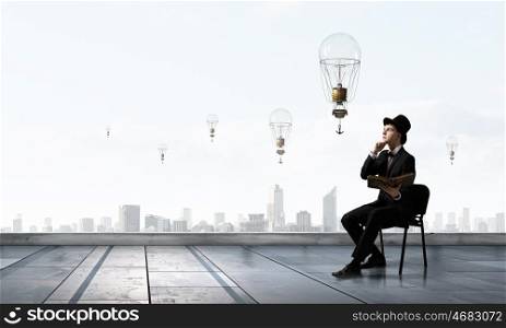 Businessman in cylinder reading book. Young businessman sitting in chair with old book in hands