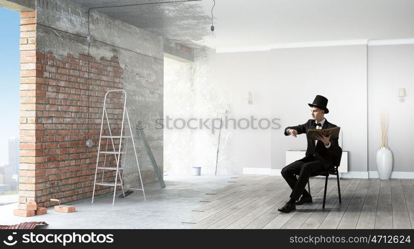 Businessman in cylinder reading book. Young businessman sitting in chair with old book in hands