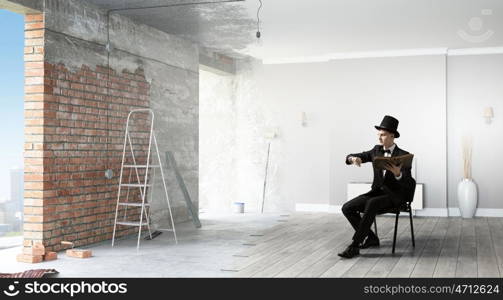 Businessman in cylinder reading book. Young businessman sitting in chair with old book in hands