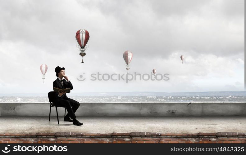 Businessman in cylinder reading book. Young businessman sitting in chair with old book in hands