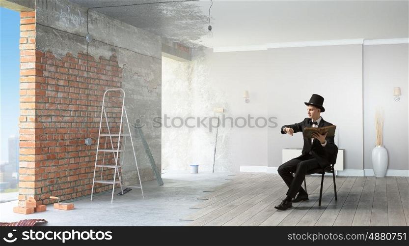 Businessman in cylinder reading book. Young businessman sitting in chair with old book in hands