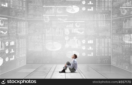 Businessman in empty room. Young businessman sitting on floor in room and infographs on wall