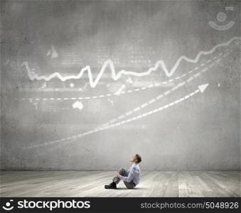 Businessman in empty room. Young businessman sitting on floor in room and infographs on wall