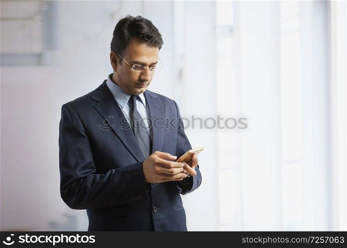 Businessman in formal clothes and eyeglasses standing in office using mobile phone