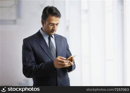 Businessman in formal clothes and eyeglasses standing in office using mobile phone