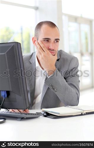 Businessman in front of desktop computer with thoughtful look