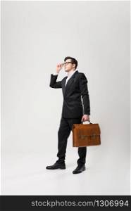 Businessman in glasses and black suit holds brown leather briefcase in hand isolated on white background