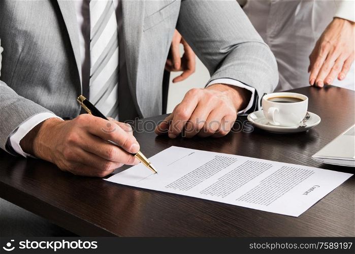 Businessman in gray suit sitting at office desk signing a contract close up. Businessman signing a contract