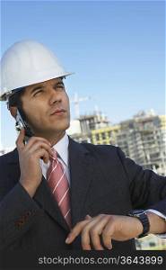 Businessman in hardhat using mobile phone, outdoors