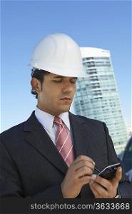 Businessman in hardhat using PDA outdoors
