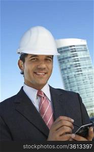 Businessman in hardhat using PDA outdoors, portrait