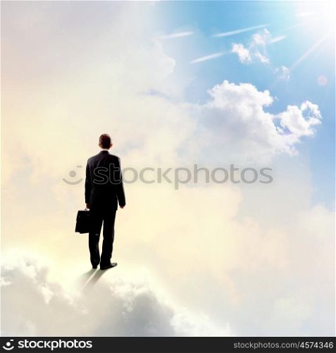 Businessman in heaven. Rear view of businessman with suitcase standing on cloud
