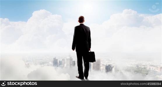 Businessman in heaven. Rear view of businessman with suitcase standing on cloud