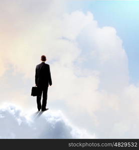 Businessman in heaven. Rear view of businessman with suitcase standing on cloud