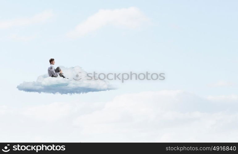 Businessman in isolation. Depressed young businessman sitting alone on cloud high in sky