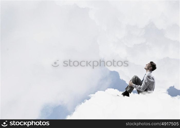 Businessman in isolation. Smiling young businessman sitting alone on cloud high in sky