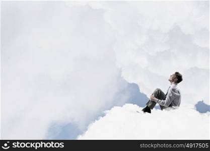Businessman in isolation. Smiling young businessman sitting alone on cloud high in sky