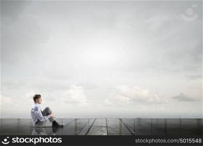 Businessman in isolation. Thoughtful businessman sitting alone on building roof